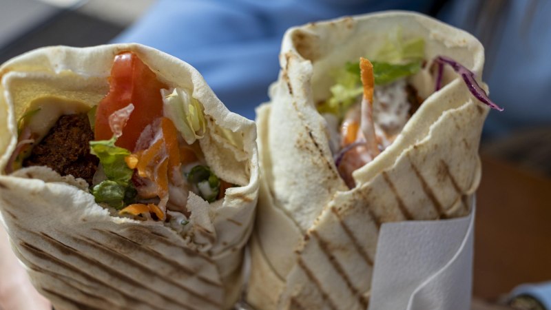 Zwei frisch gegrillte Wraps, gefüllt mit Falafel, Salat, Tomaten und Joghurtsoße, werden in der Hand gehalten. Die knusprigen Fladenbrote sind mit Grillstreifen versehen. Die Wraps sind im Fokus, im Hintergrund verschwommen erkennt man die blauen Ärmel der Person, die die Wraps hält. , © Stuttgart-Marketing GmbH, Sarah Schmid