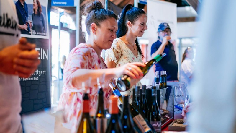 Zwei Frauen schenken Wein bei einer Verkostung ein, umgeben von Weinflaschen. Im Hintergrund probieren weitere Gäste Weine an einem Stand., © Stuttgart-Marketing GmbH, Thomas Niedermüller